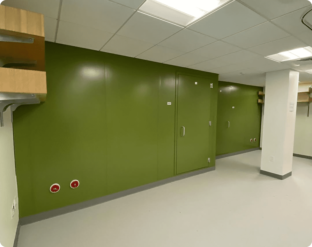 Room with green lockers and a white floor, illuminated by lights from the ceiling