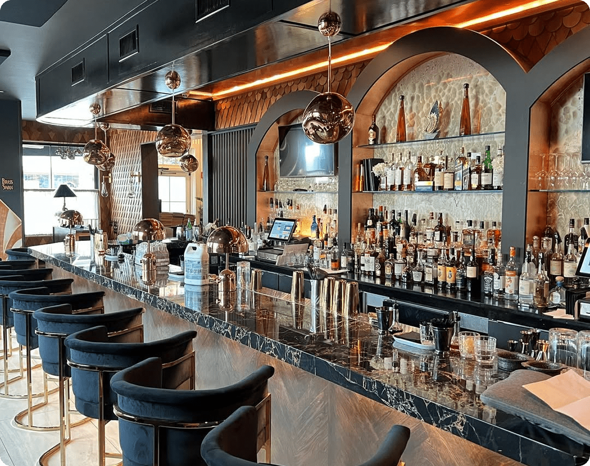 Bar with blue chairs and a marble counter top, surrounded by bottles arranged in racks, glasses, plates