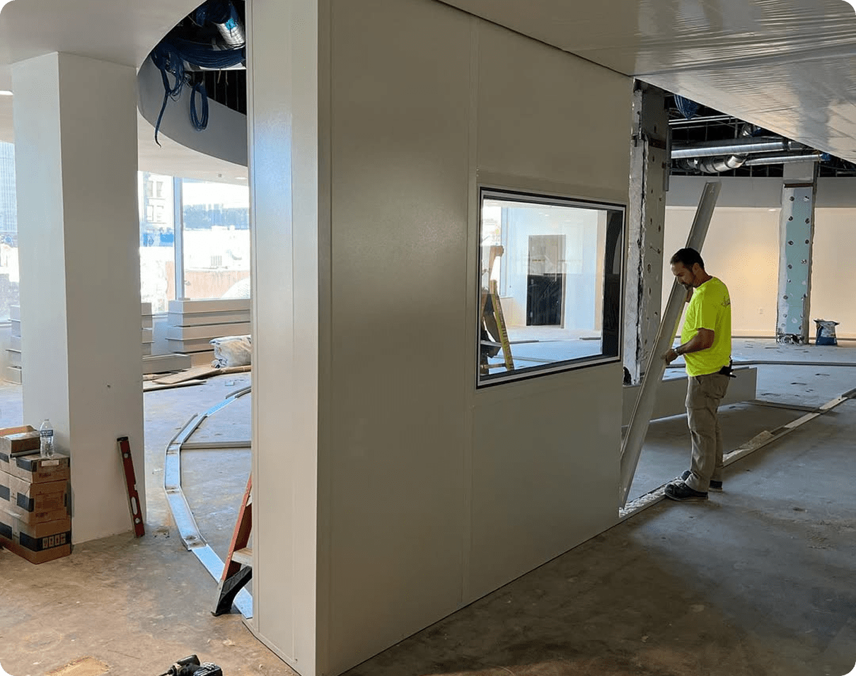 Man in a shirt standing on a ladder in a room with a wall featuring a glass window, pillars
