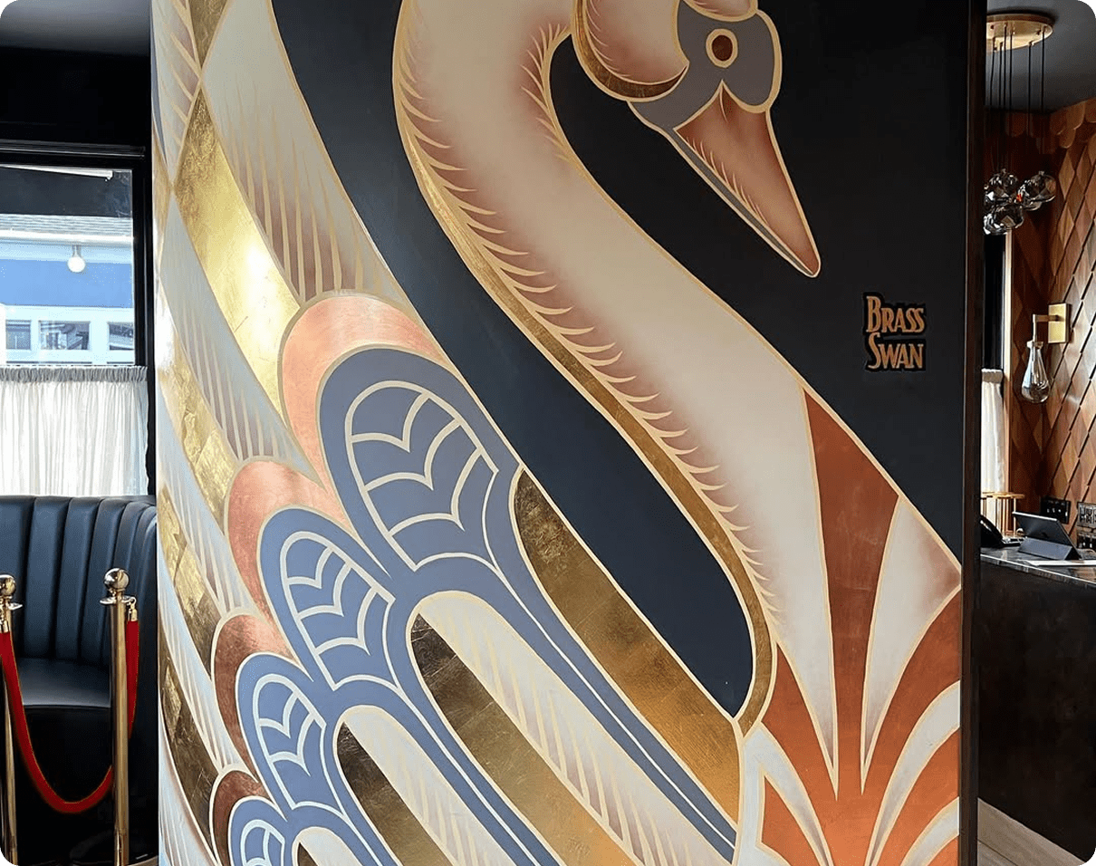 Large mural of a swan painted on the side of a building, with a sofa, barrier poles, lights